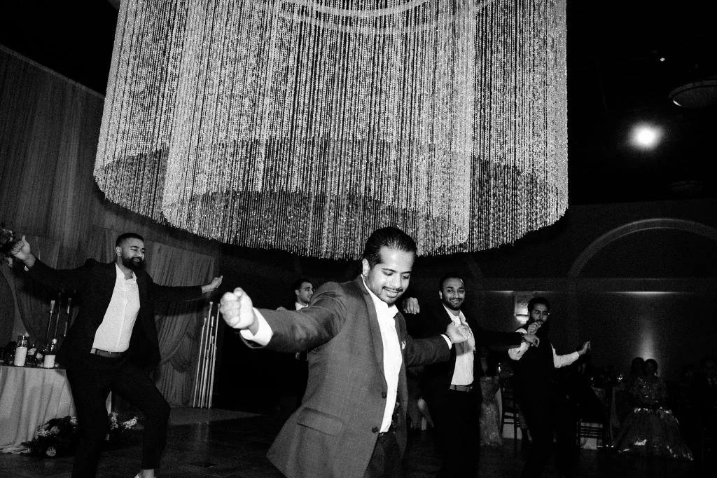Wedding guests dancing together beneath a chandelier at the reception