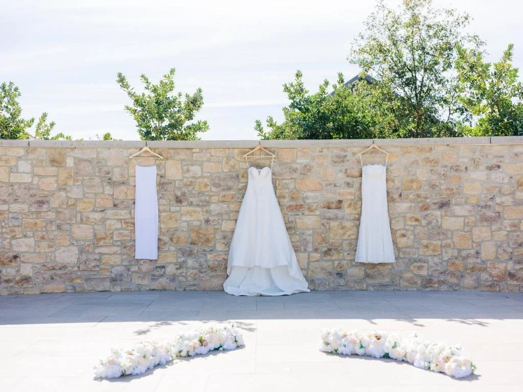 Wedding dress and additional dresses hanging beside a floral arrangement