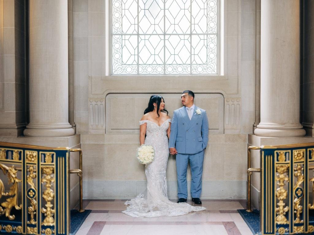 Bride and groom standing beneath a stained glass window and looking at each other inside San Francisco City Hall