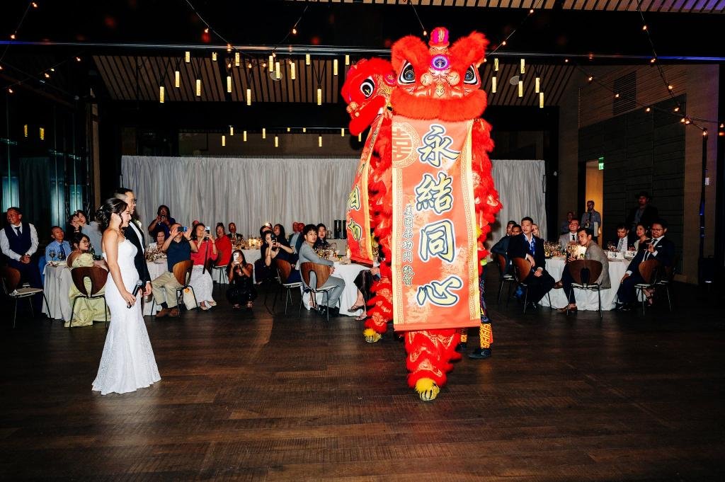 Bride and groom standing with a lion dance performer in front of their reception guests