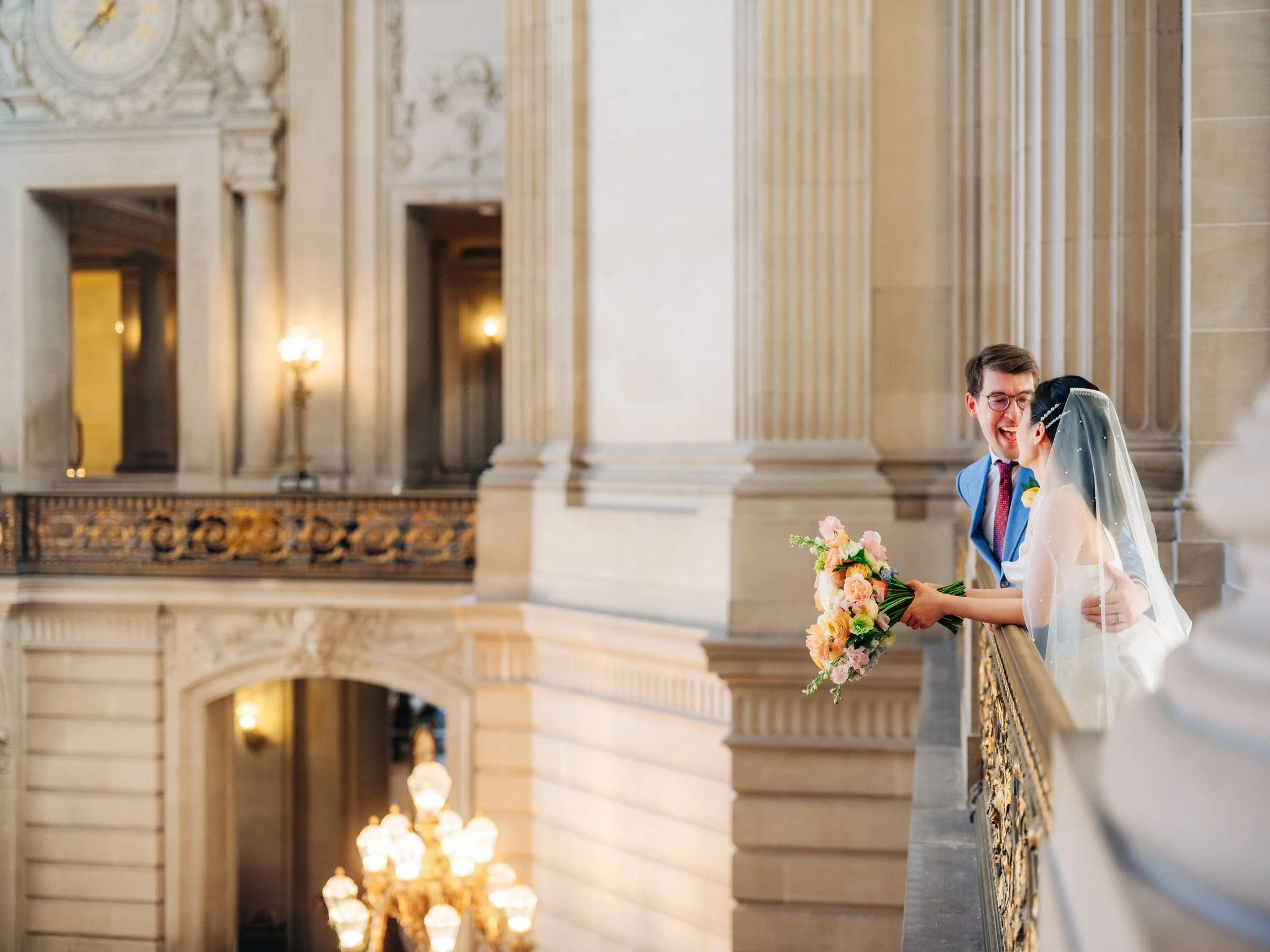 Bride and groom leaning over balcony smiling at each other at San Francisco City Hall wedding