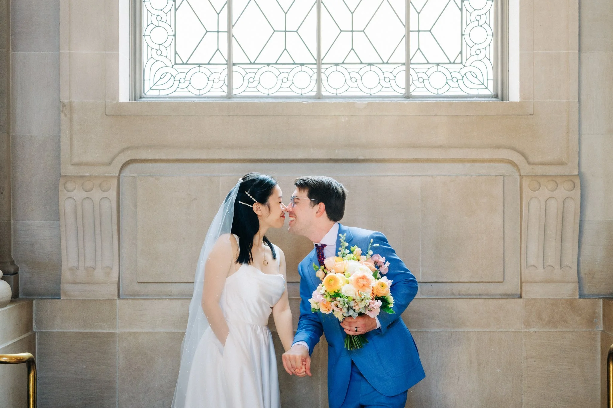 Bride and groom touching noses in front of large window at San Francisco City Hall wedding