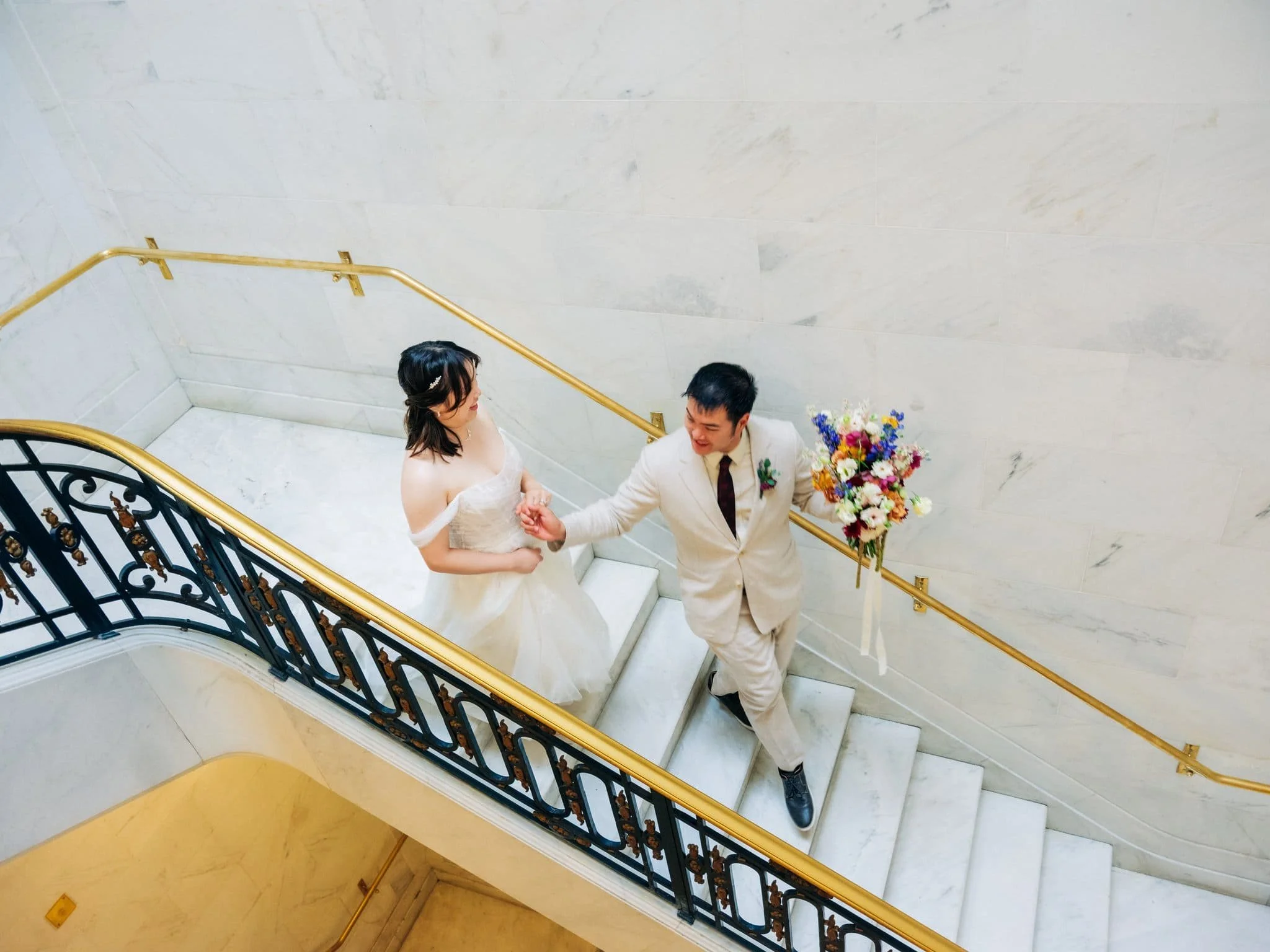 Groom holding the bride’s hand as they walk down the stairs during their San Francisco City Hall elopement.