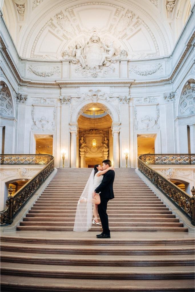 Bride jumping into the groom's arms for a kiss at the bottom of the City Hall staircase