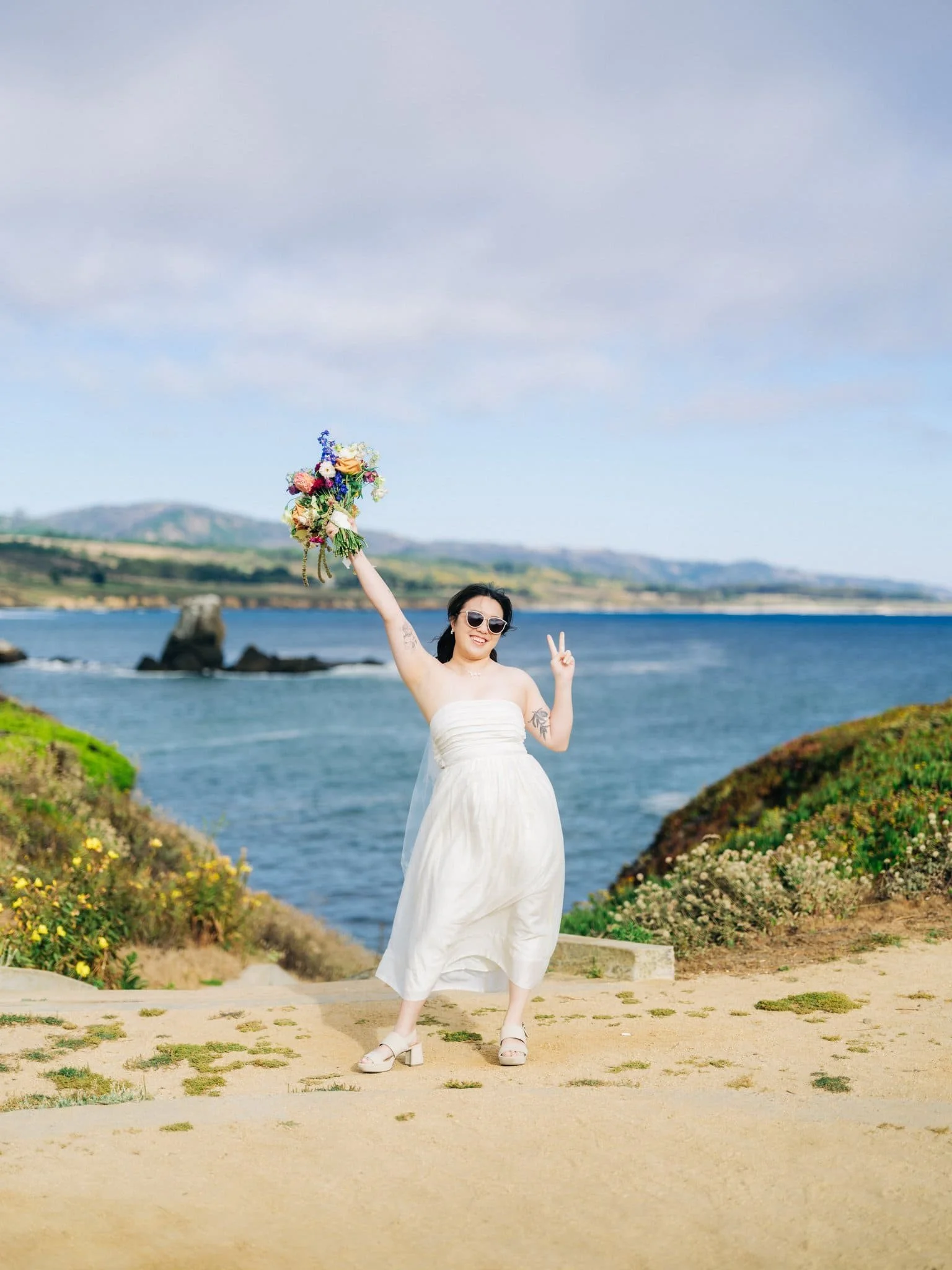 Bride posing with her bouquet above her head along the coast during her Pigeon Point Lighthouse elopement.
