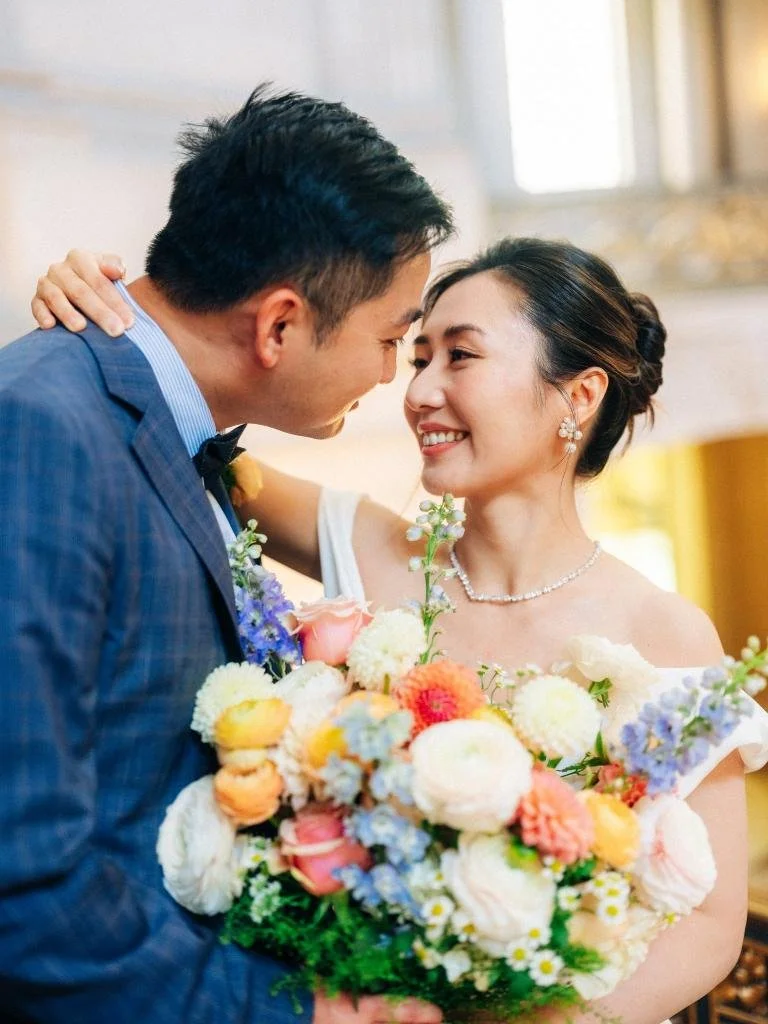 Bride with her arm around the groom while holding her bouquet during their San Francisco City Hall elopement.