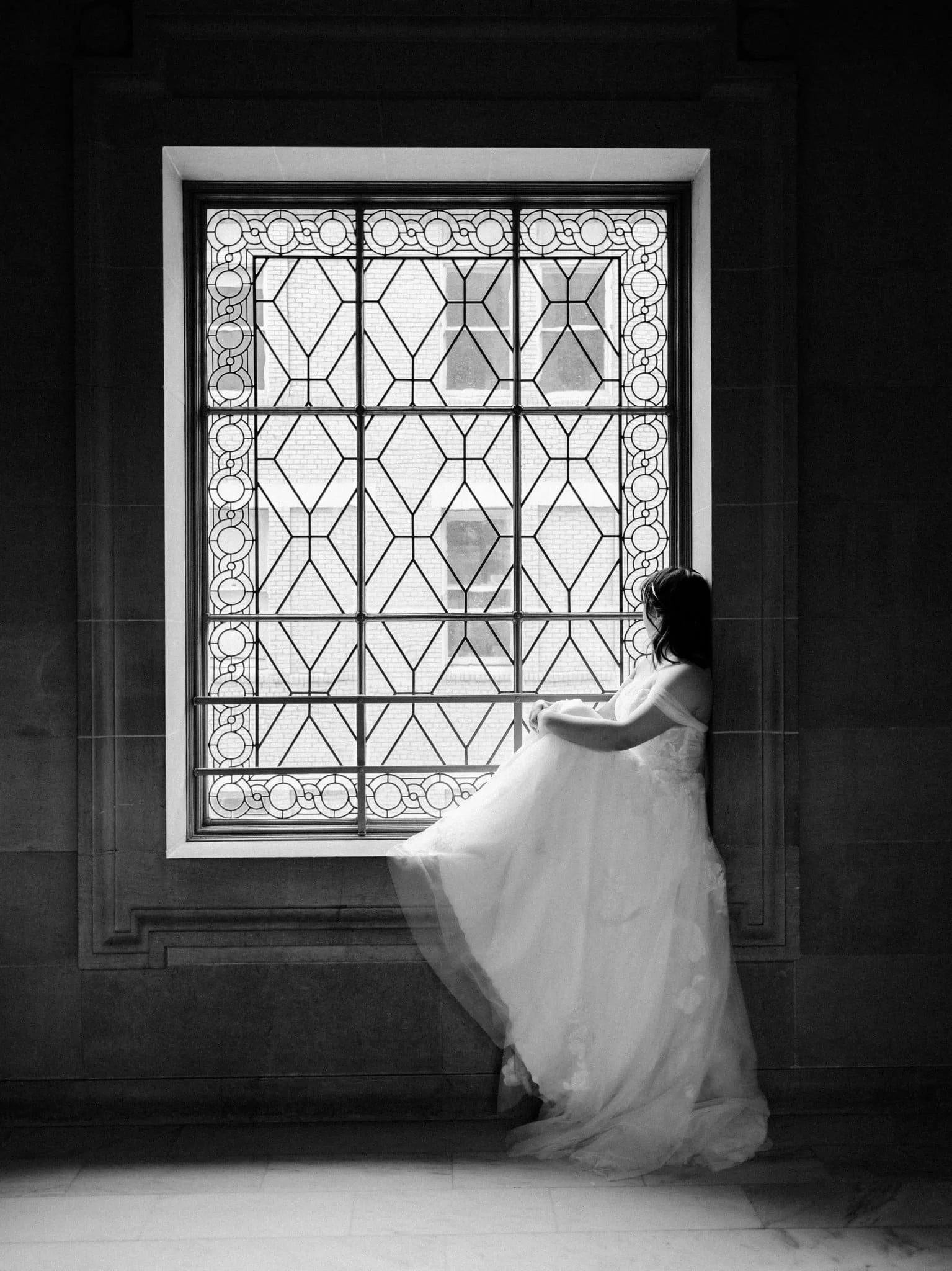 Bride sitting on a windowsill in front of a stained glass window at San Francisco City Hall.