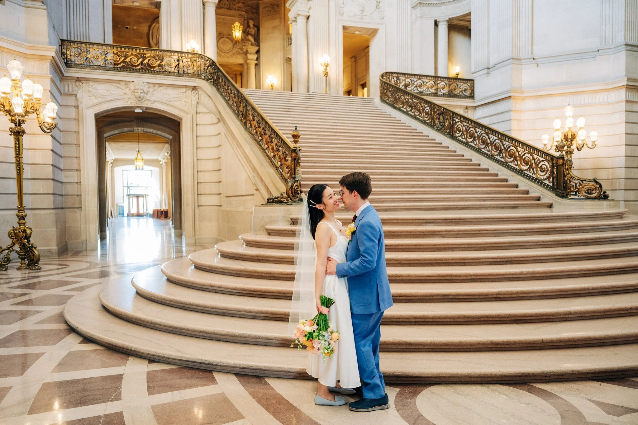 Bride and groom embracing at bottom of staircase at San Francisco City Hall wedding