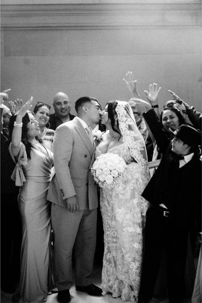 Bride and groom kissing while guests celebrate behind them.