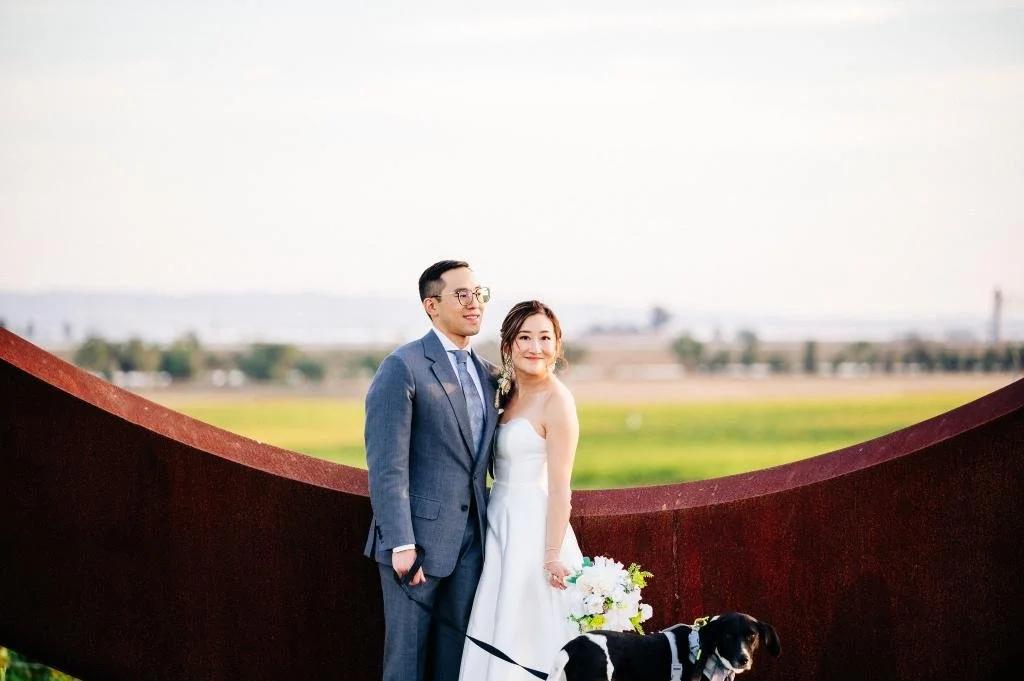 Bride and groom posing with their dog beside a sculpture at Stanly Ranch