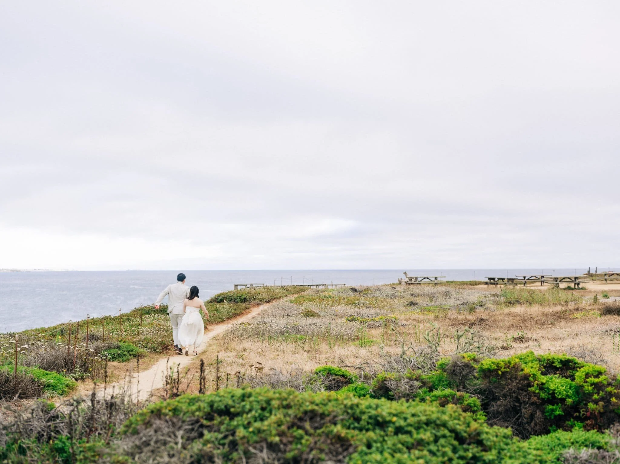 Bride and groom walking down a coastal path during their Pigeon Point Lighthouse elopement.