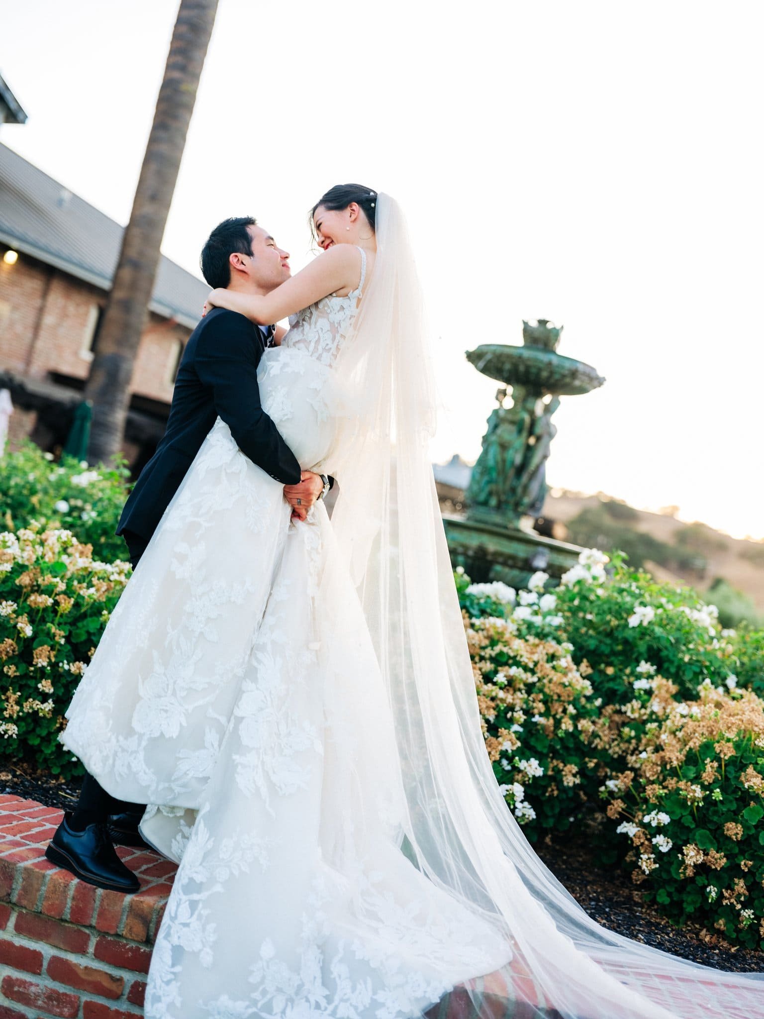 groom lifting bride in embrace with fountain behind them palm event center pleasanton wedding