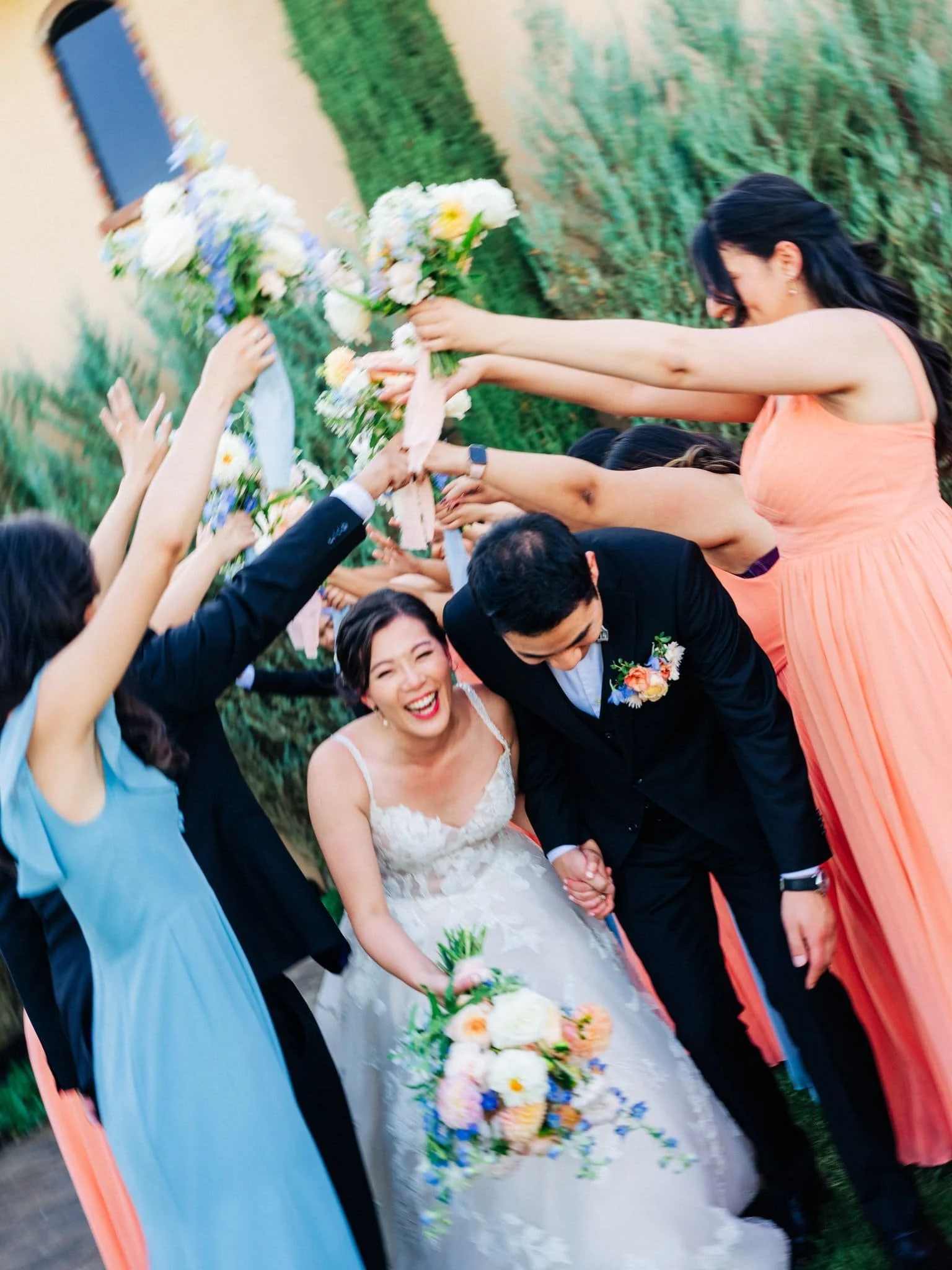 bridesmaids holding flowers up like arch as bride and groom walk underneath smiling palm event center pleasanton wedding