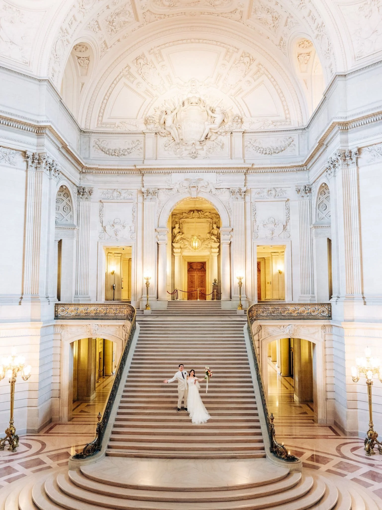 Bride and groom posing with arms wide on the grand staircase during their San Francisco City Hall elopement.