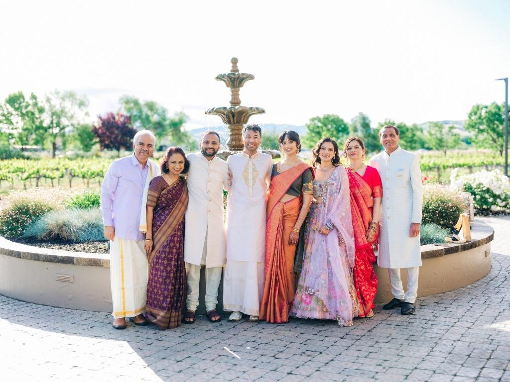 Bride and groom posing with their parents in front of a fountain