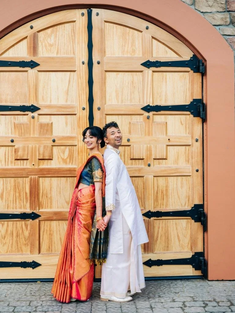 Bride and groom standing back to back in front of a large doorway before their Indian wedding