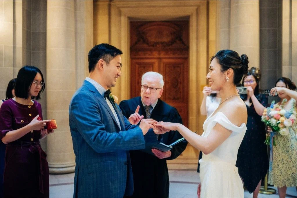 Bride placing a wedding ring on the groom's finger during their San Francisco City Hall ceremony.