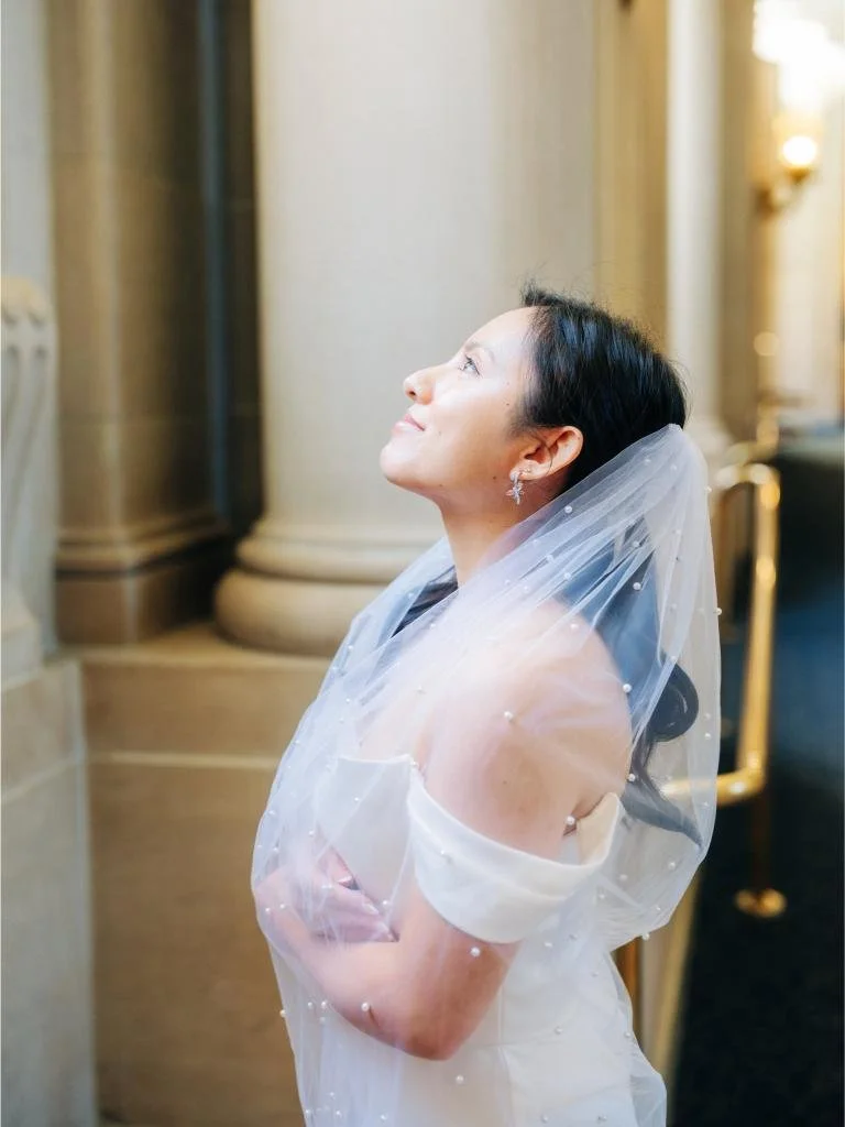 Bride smiling while looking up and holding her veil inside San Francisco City Hall
