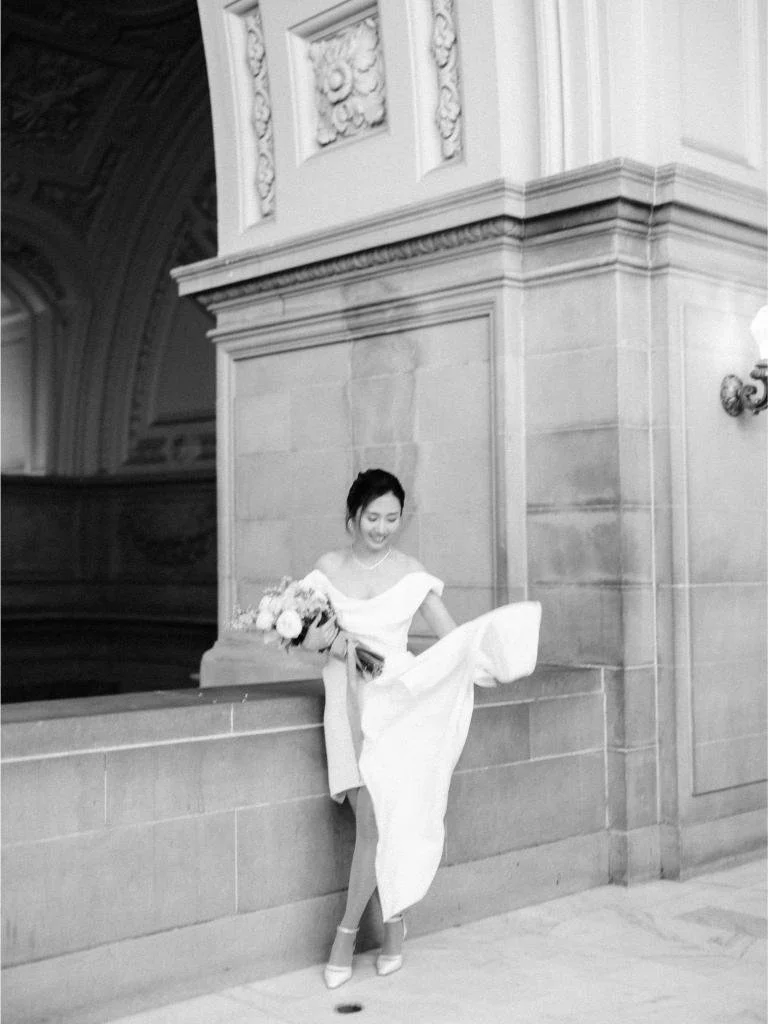 Bride standing beneath an ornate archway at San Francisco City Hall holding her bouquet.