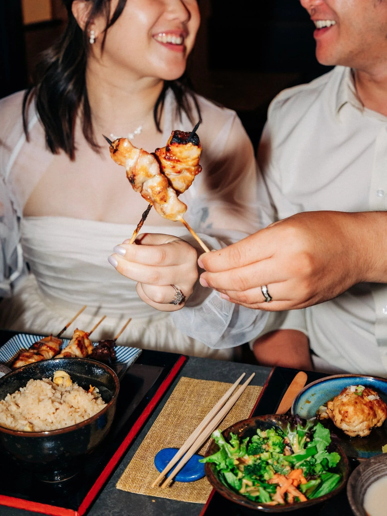 Bride and groom cheering with chicken skewers during dinner at Yakitori Edomasa in San Francisco Japantown after their elopement.