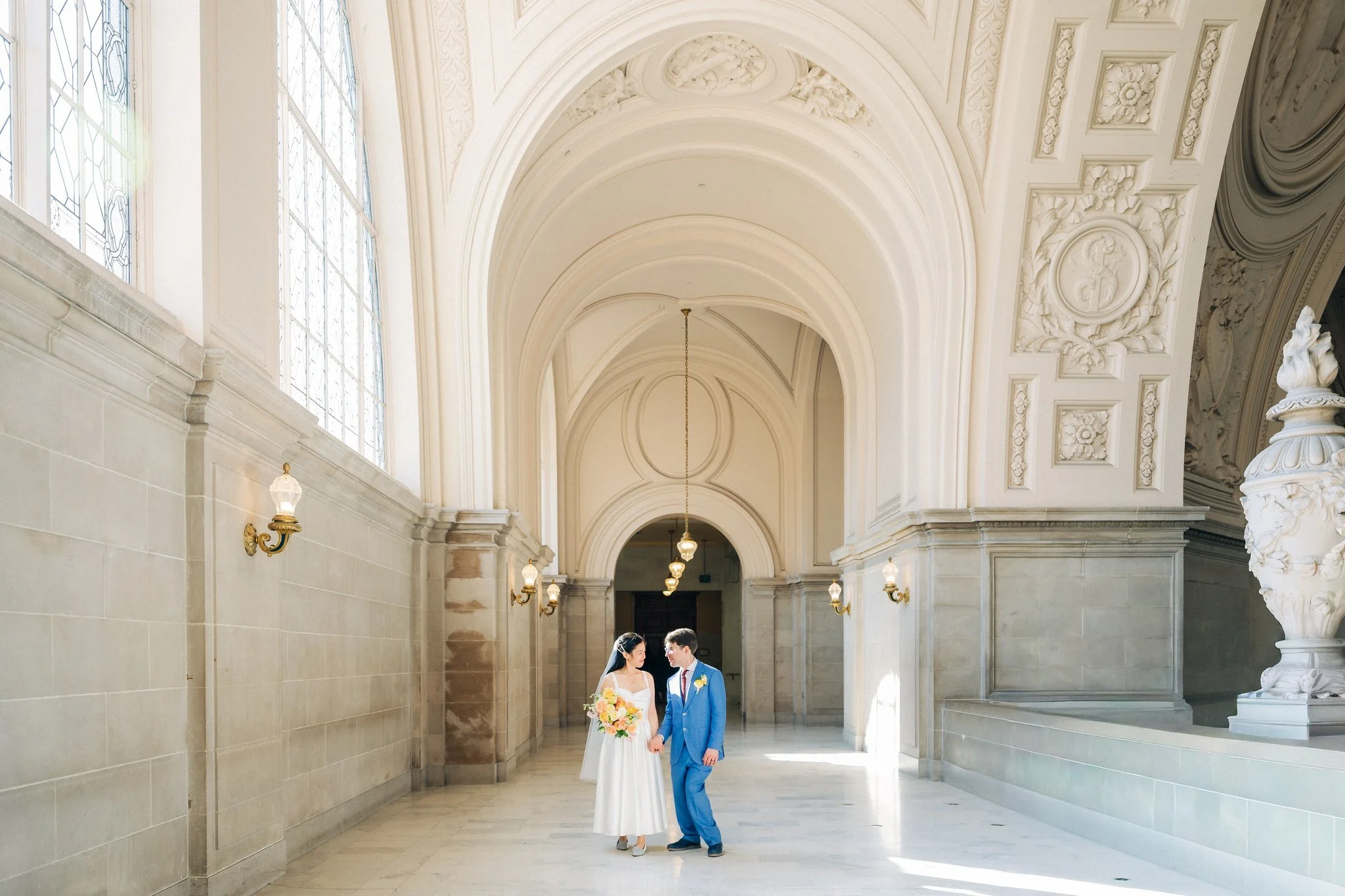 Bride and groom looking at each other in hallway with archway at San Francisco City Hall wedding