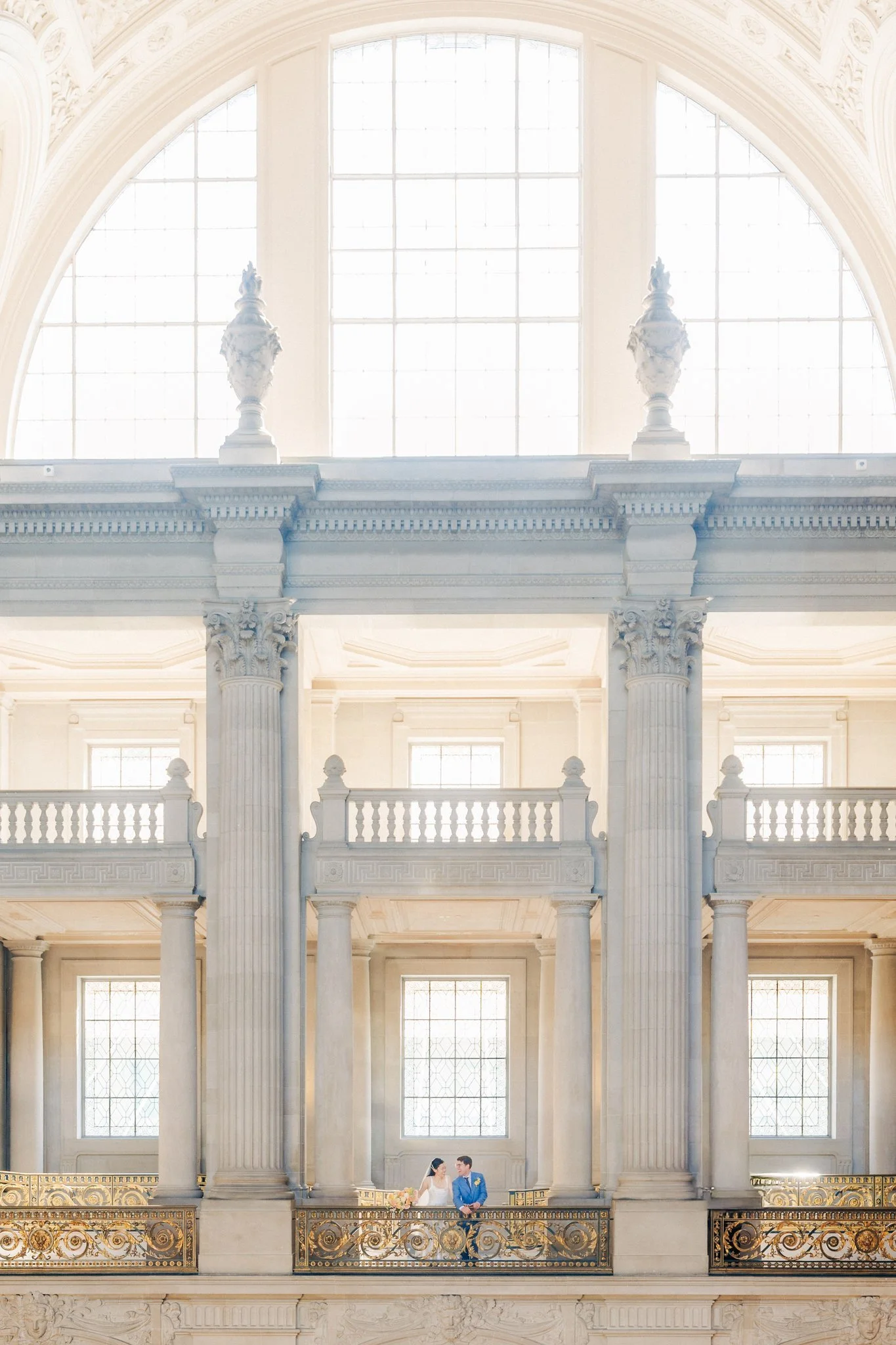 Wide shot of couple on balcony with large archway and windows at San Francisco City Hall wedding