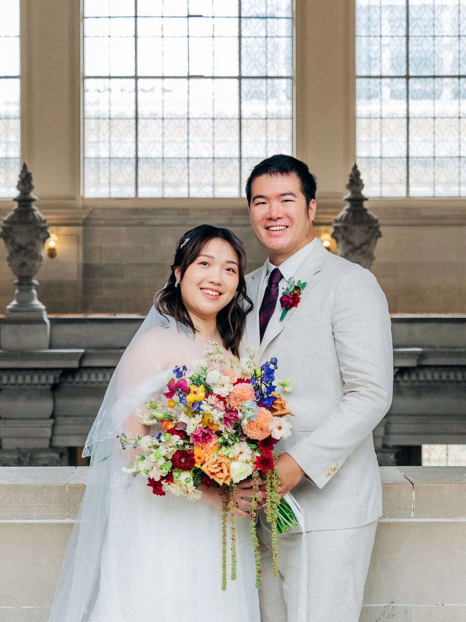 Bride and groom posing with the bride’s bouquet on a balcony during their San Francisco City Hall elopement.