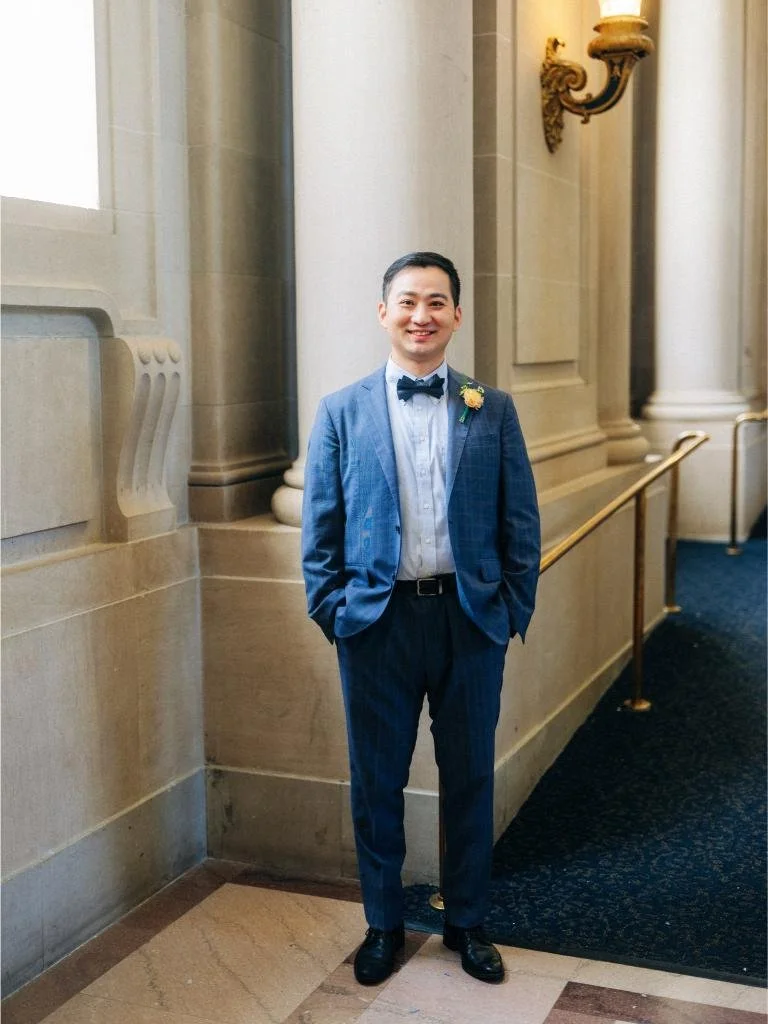 Groom posing in a San Francisco City Hall hallway wearing a blue suit and bow tie.