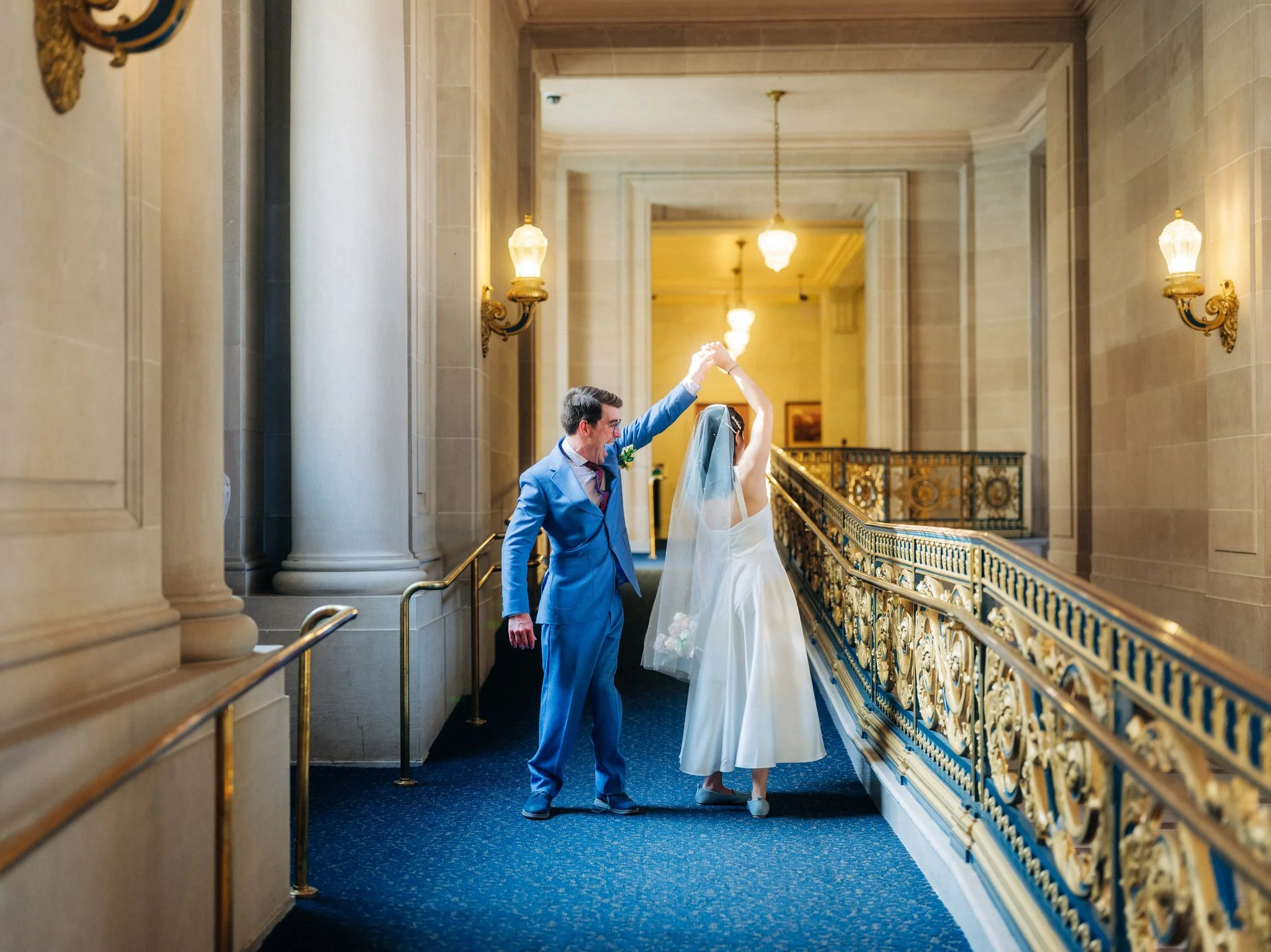 Groom twirling bride in hallway with gold railings at San Francisco City Hall wedding