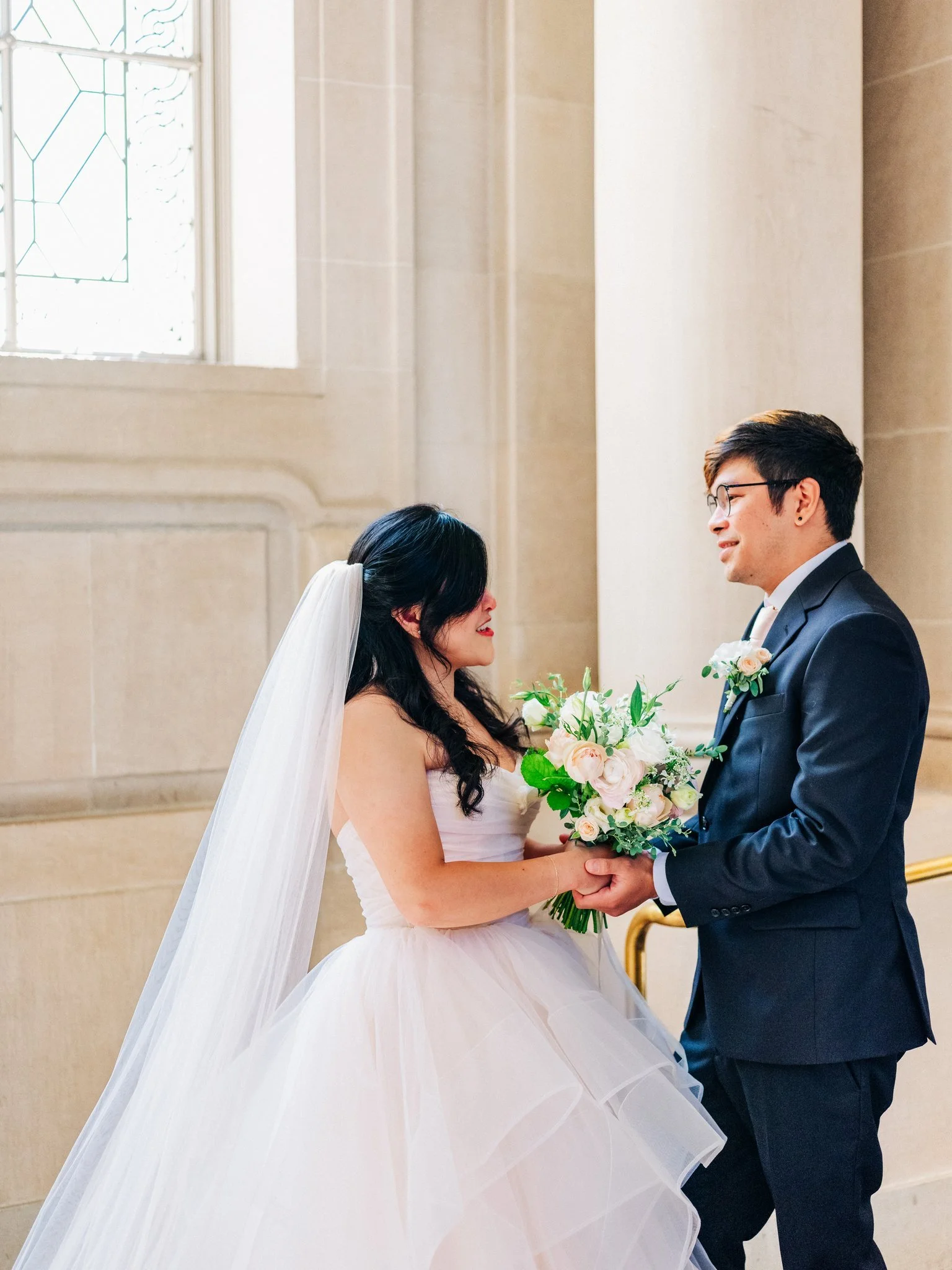 Bride and groom holding hands over bouquet in hallway at San Francisco City Hall wedding