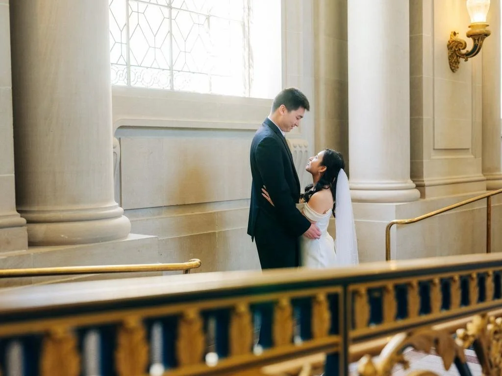 Bride looking up at the groom beside the golden staircase at San Francisco City Hall
