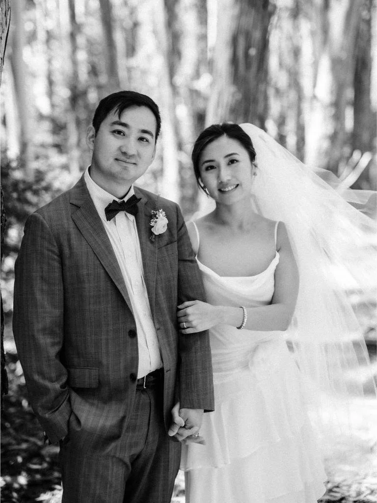 Newlyweds holding hands and smiling at the camera with trees behind them at Lover's Lane in the Presidio.