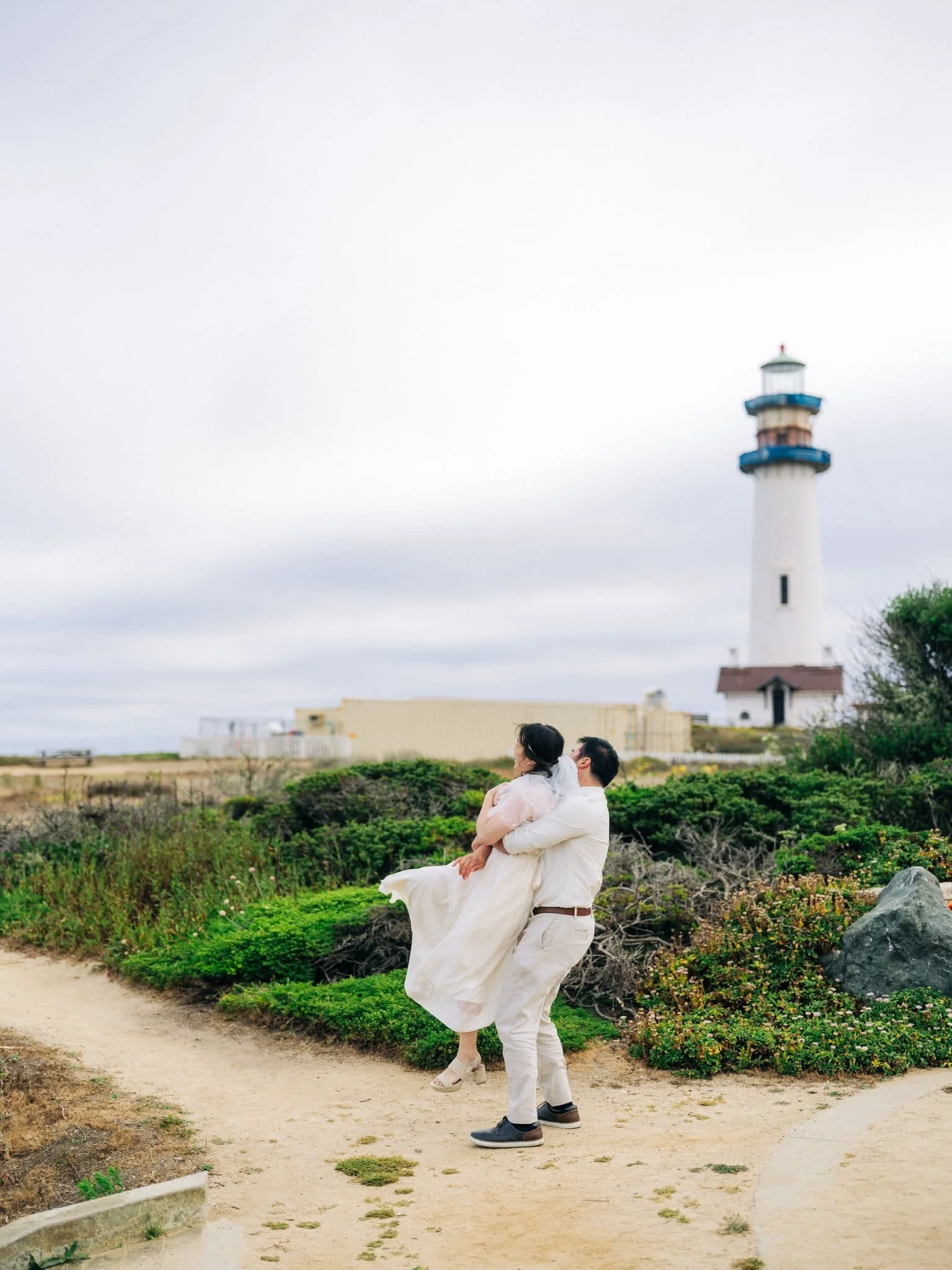 Groom lifting the bride with Pigeon Point Lighthouse in the background during their coastal elopement.