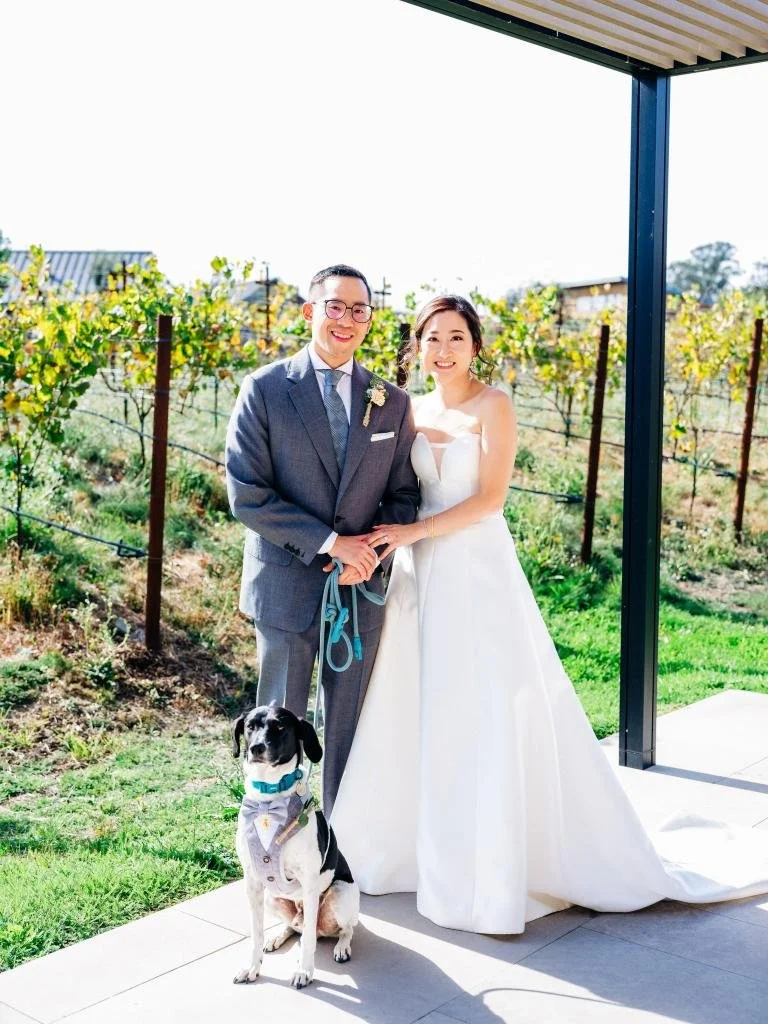 Bride and groom posing with their dog with vineyards behind them at Stanly Ranch