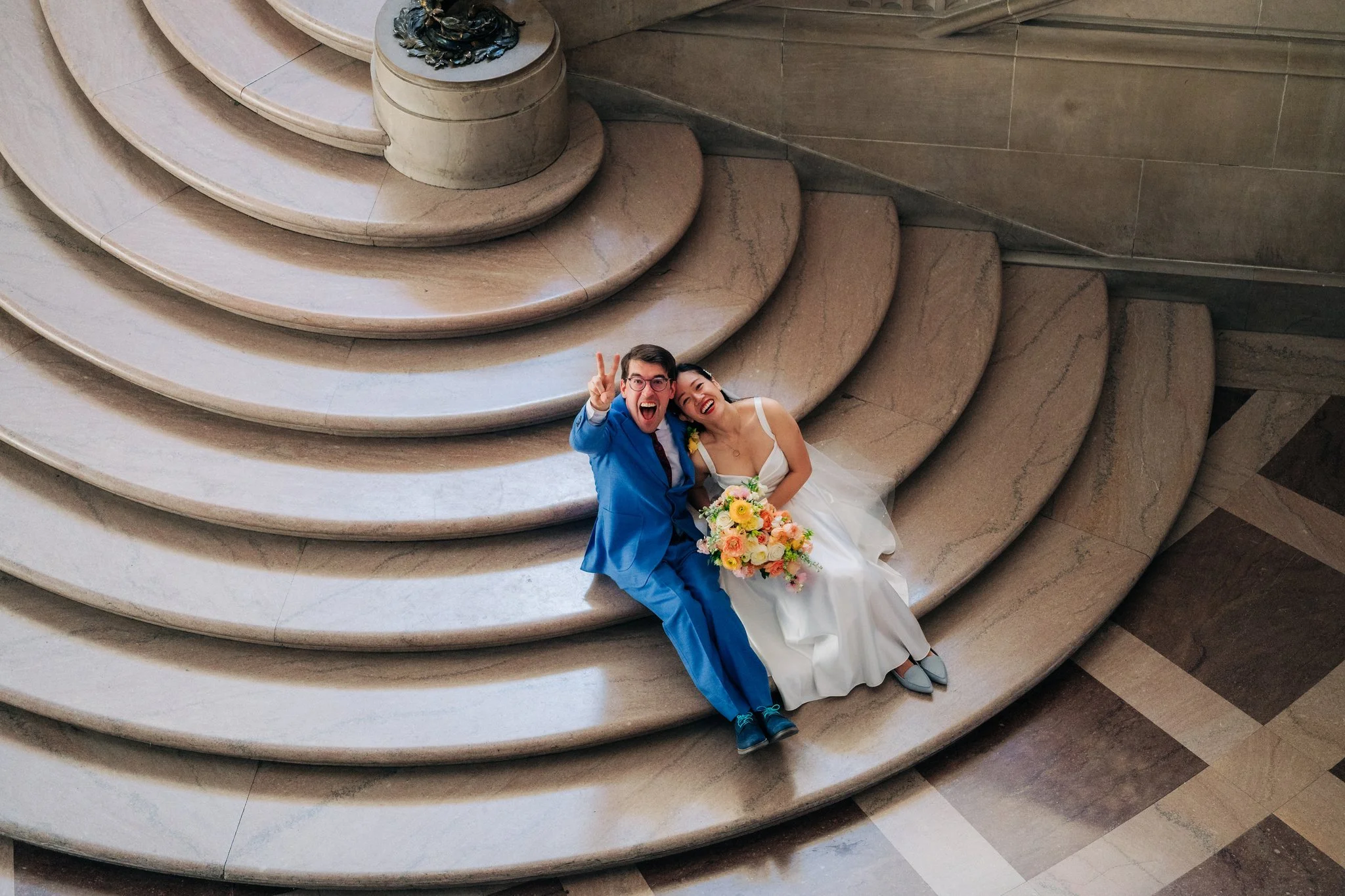 Bride and groom looking up at camera from bottom of staircase at San Francisco City Hall wedding