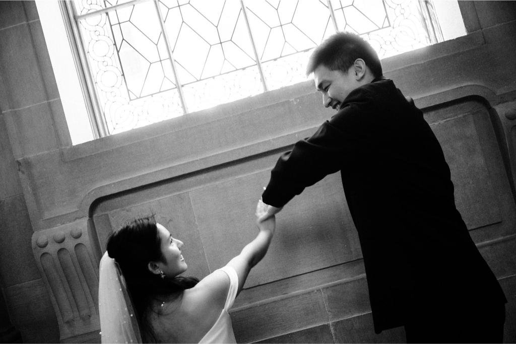Groom twirling the bride beside a stained glass window at San Francisco City Hall