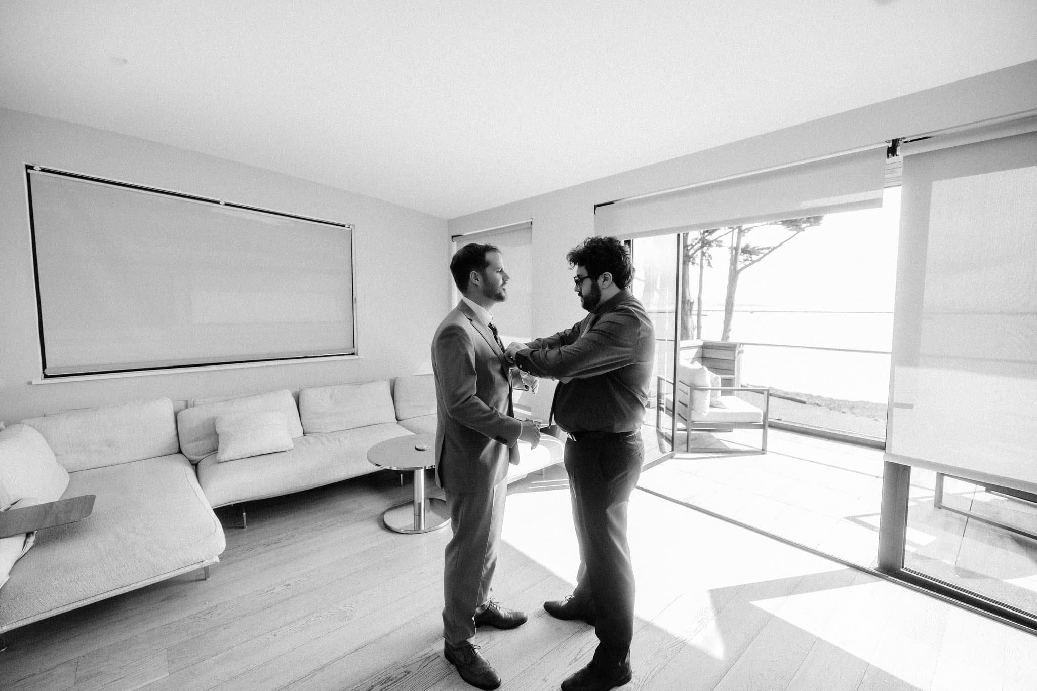 Best man helping the groom button his suit jacket while getting ready for their Half Moon Bay wedding