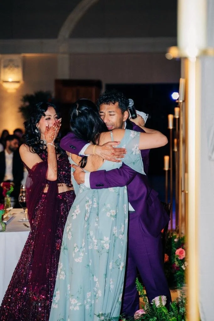 Bride and groom embracing a guest after a reception speech