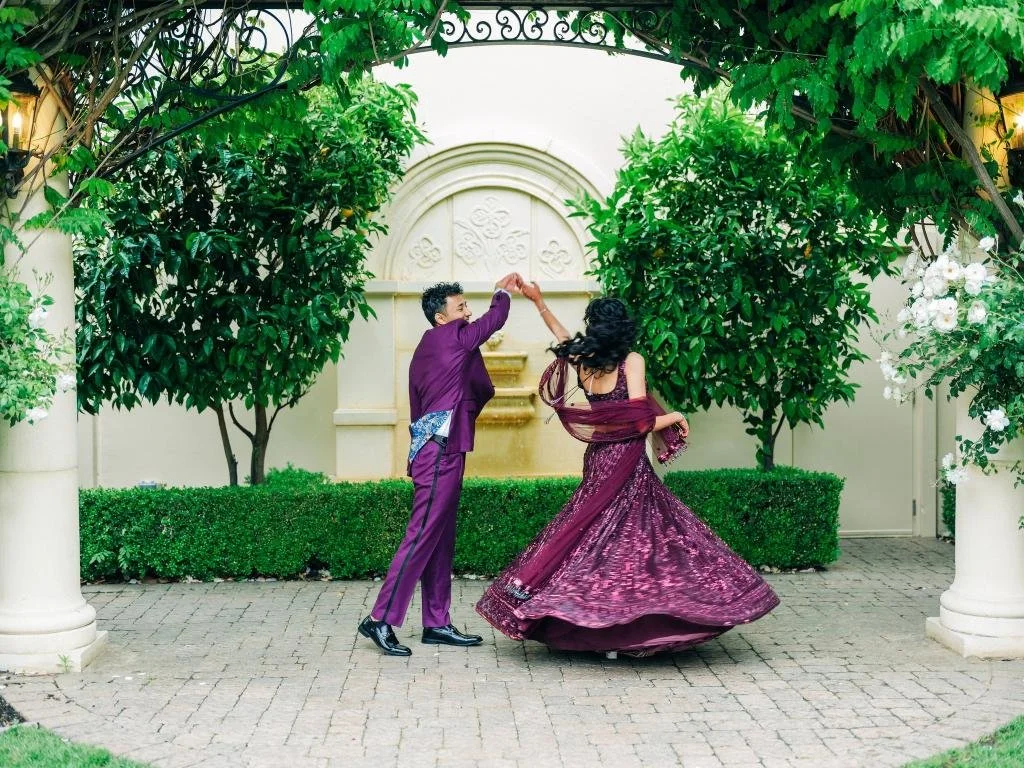 Groom twirling the bride on the dance floor in coordinating purple reception attire
