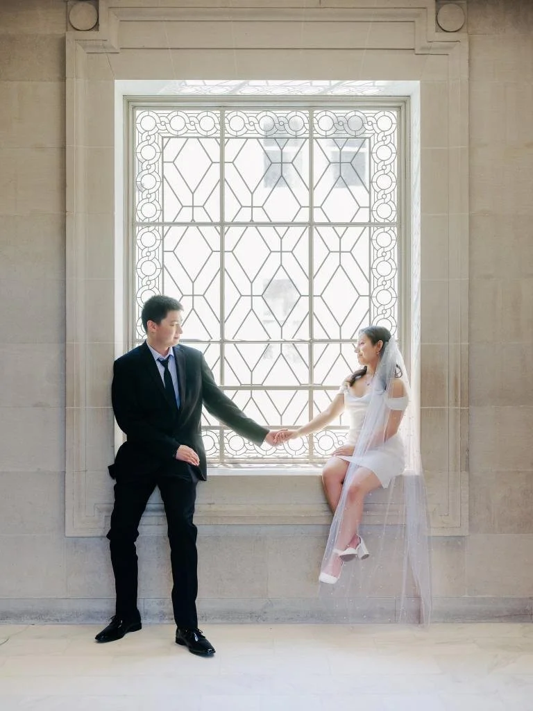 Bride and groom sitting on a window sill holding hands at San Francisco City Hall