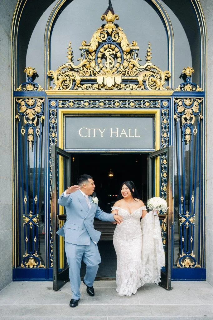 Excited newlyweds walking out the front doors beneath the City Hall sign in San Francisco