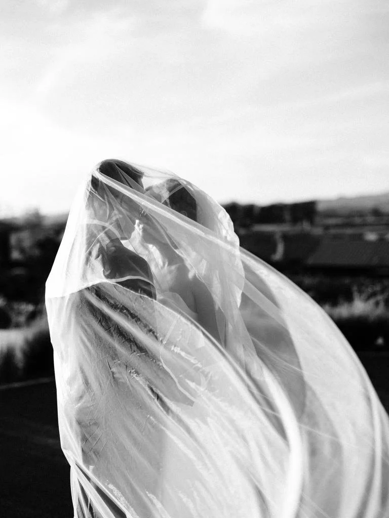 Bride and groom posing together with her veil wrapped around them