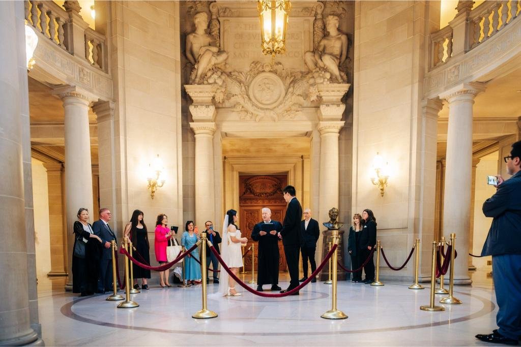 Bride and groom listening during their San Francisco City Hall civil ceremony with family gathered around them