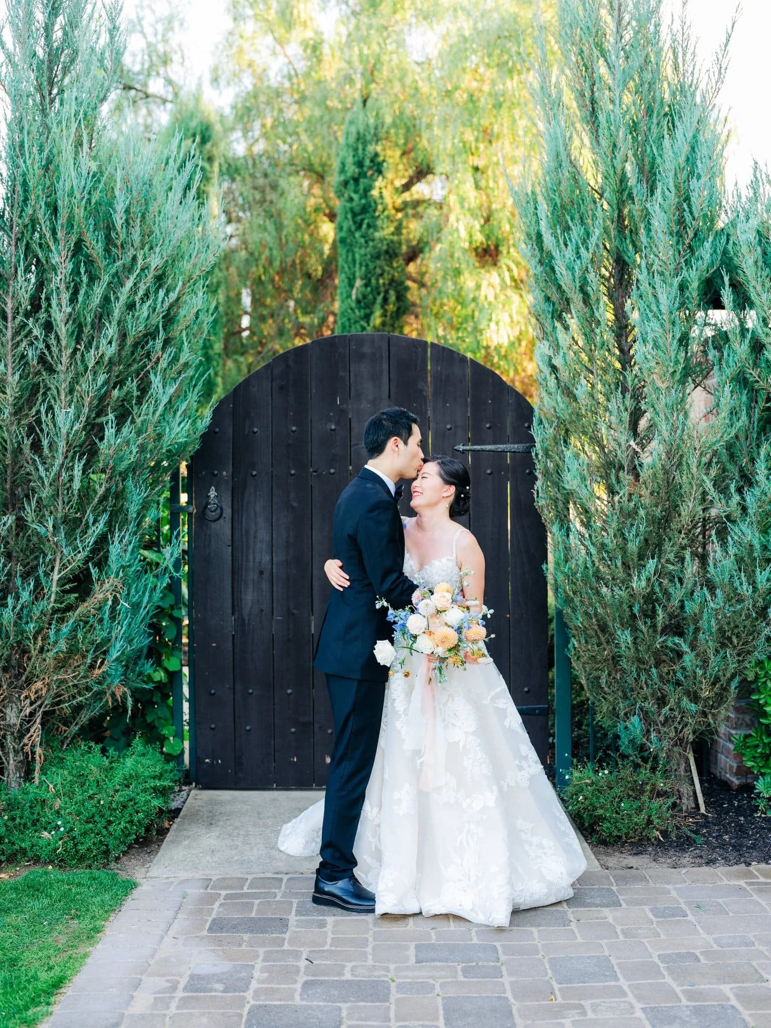 bride and groom embracing on path with black gate behind them palm event center pleasanton wedding