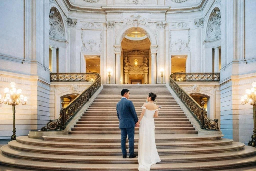Bride and groom photographed from behind at the bottom of the San Francisco City Hall grand staircase.