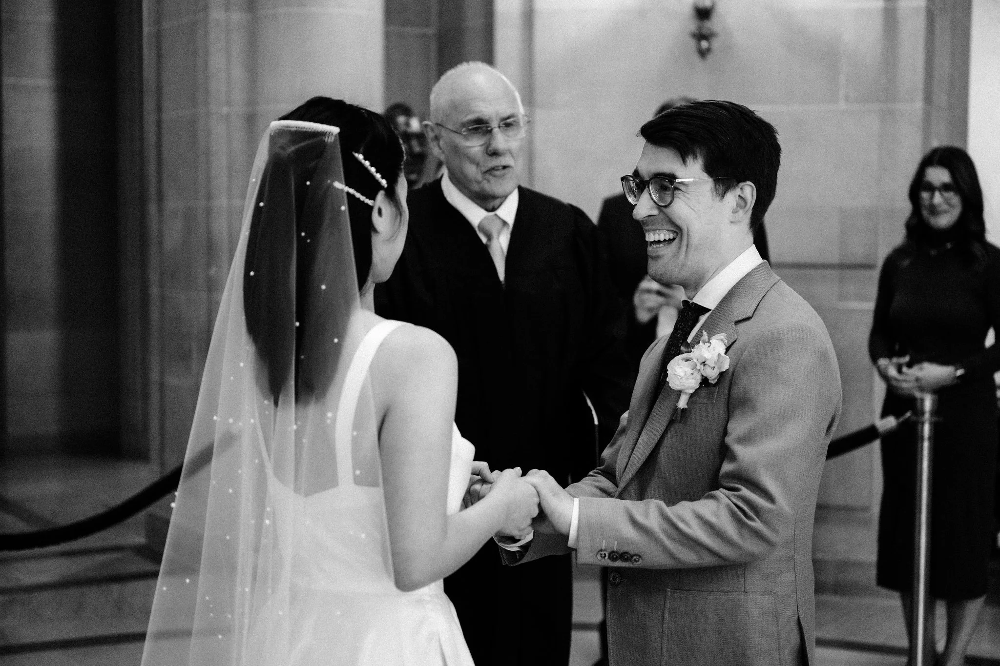 Bride and groom holding hands in front of officiant during San Francisco City Hall wedding ceremony
