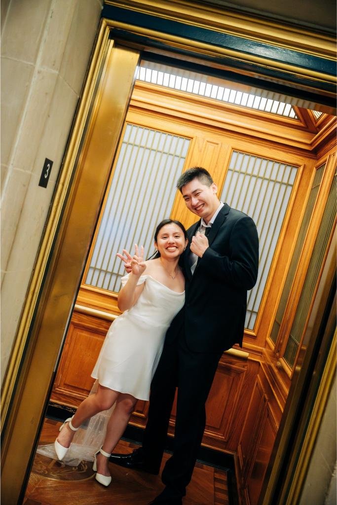 Bride and groom smiling in the elevator and giving a peace sign after their City Hall wedding
