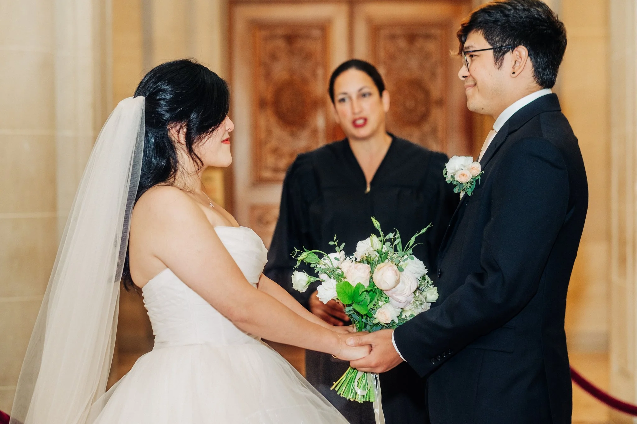Bride and groom holding hands in front of officiant during San Francisco City Hall wedding ceremony