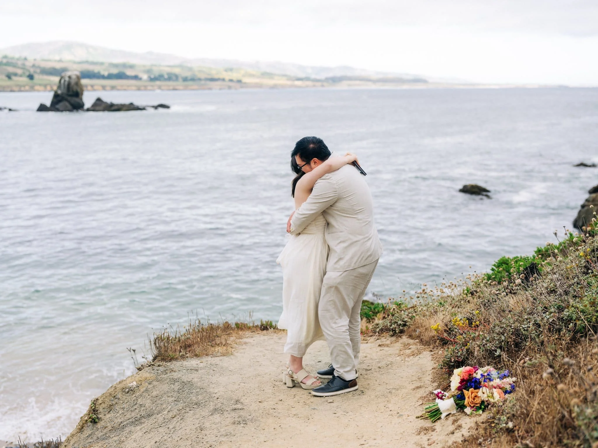 Bride and groom embracing on the coast during their Pigeon Point Lighthouse elopement.