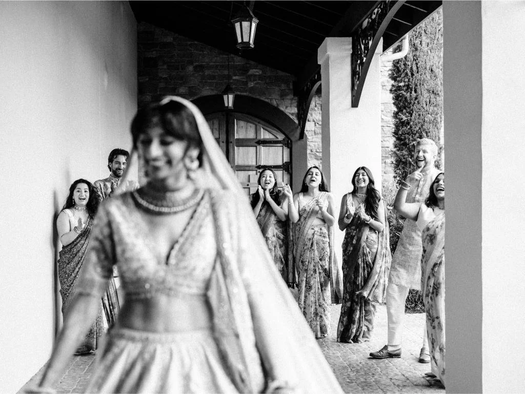 Bride in her wedding attire with bridesmaids behind her while getting ready